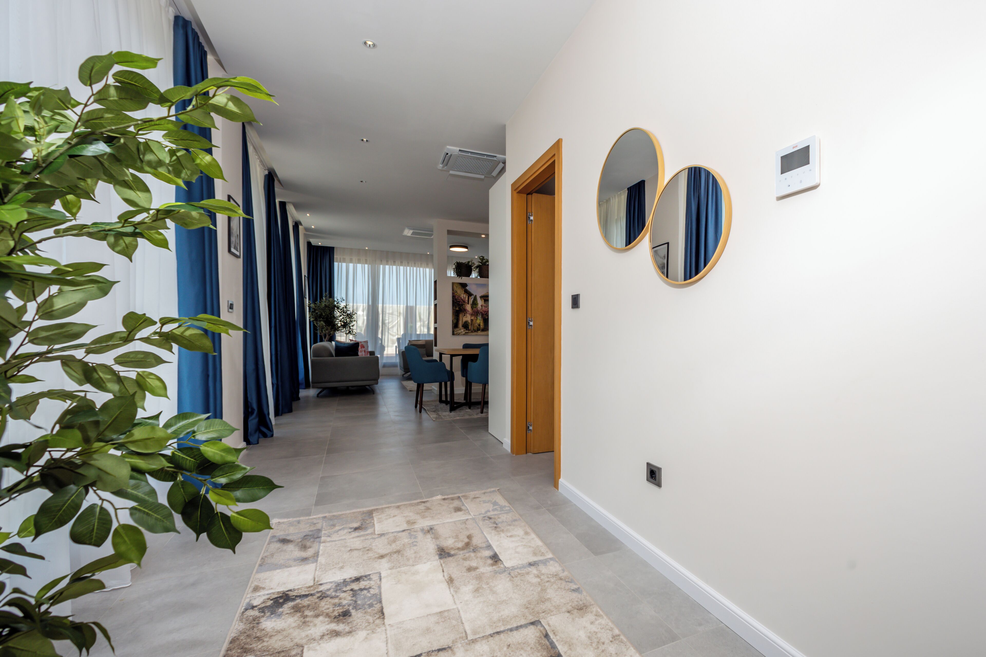 A modern hotel corridor with a dining area, a wooden door, and a thermostat on the wall.