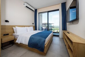 A modern hotel room with a large bed, a TV, a desk, and a balcony with a view. - Royal Blue Resort & Residence (Kotor)