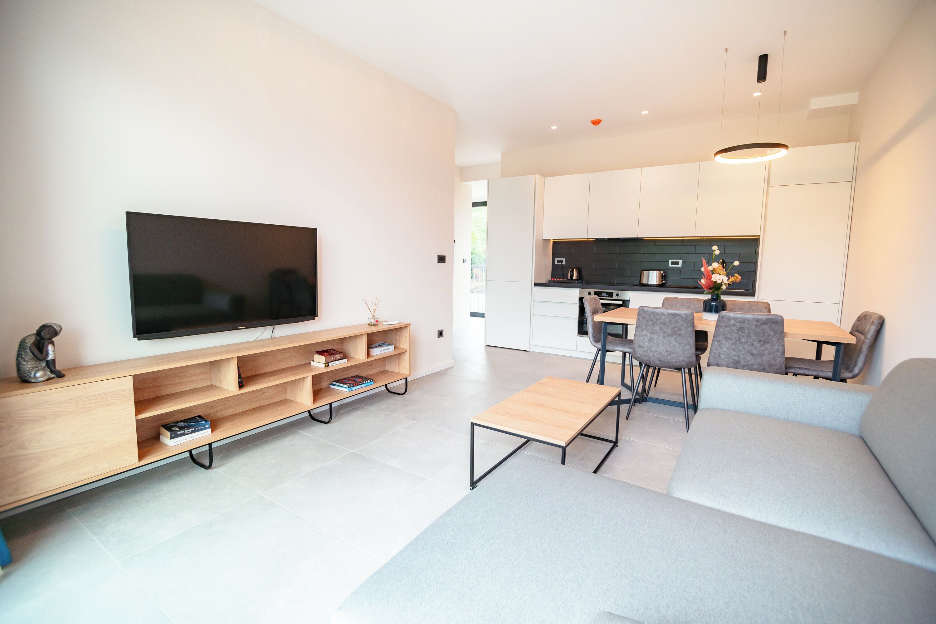 En moderne stue med et fladskærms-tv, en træunderholdningsenhed, en grå sofa og et spiseområde med stole og et bord.