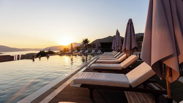 A poolside area with lounge chairs and umbrellas, overlooking a body of water and mountains during sunset. - Royal Blue Resort & Residence (Kotor)