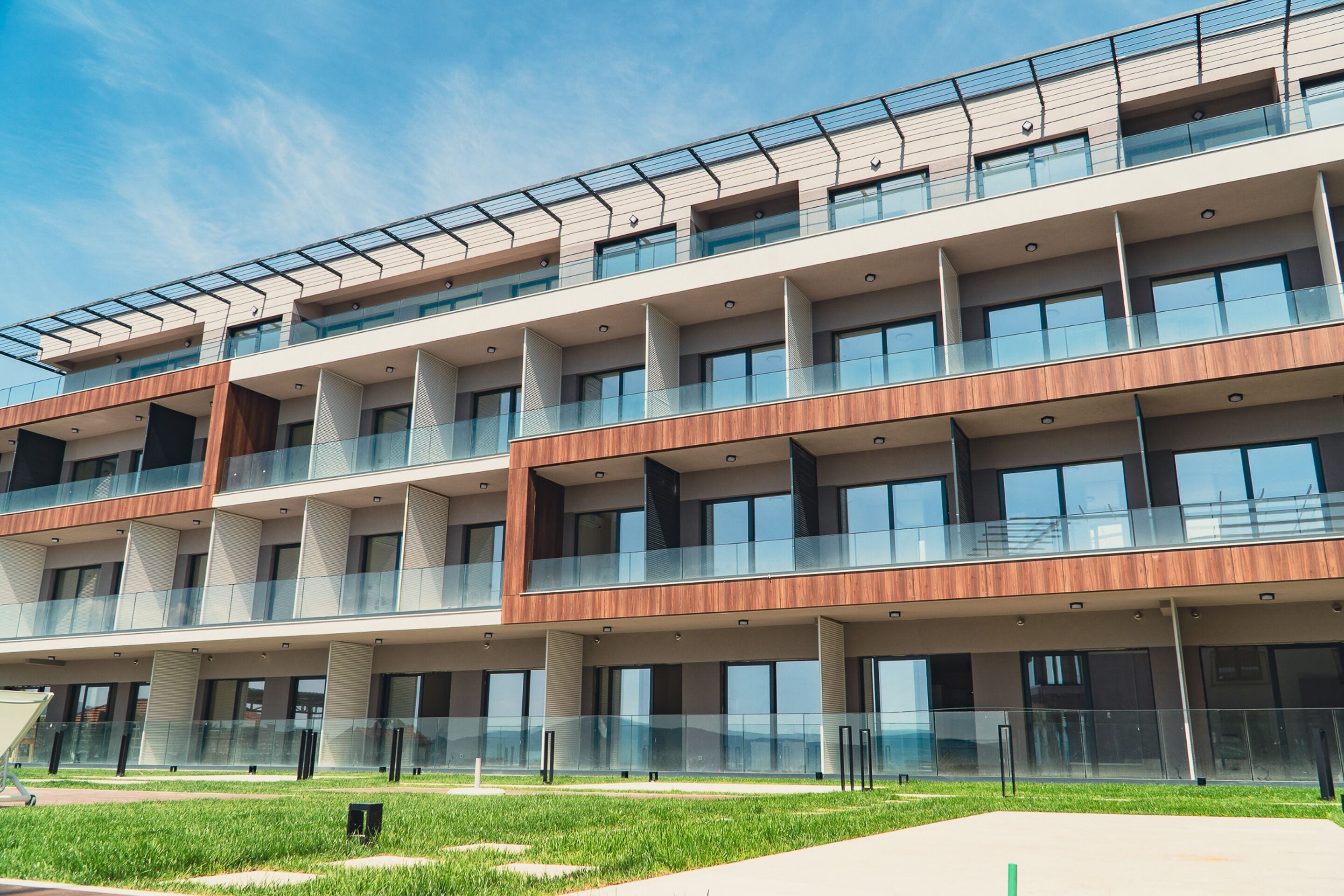 Un edificio de varios pisos con un diseño arquitectónico moderno, que cuenta con balcones con barandillas de cristal y ventanas amplias.