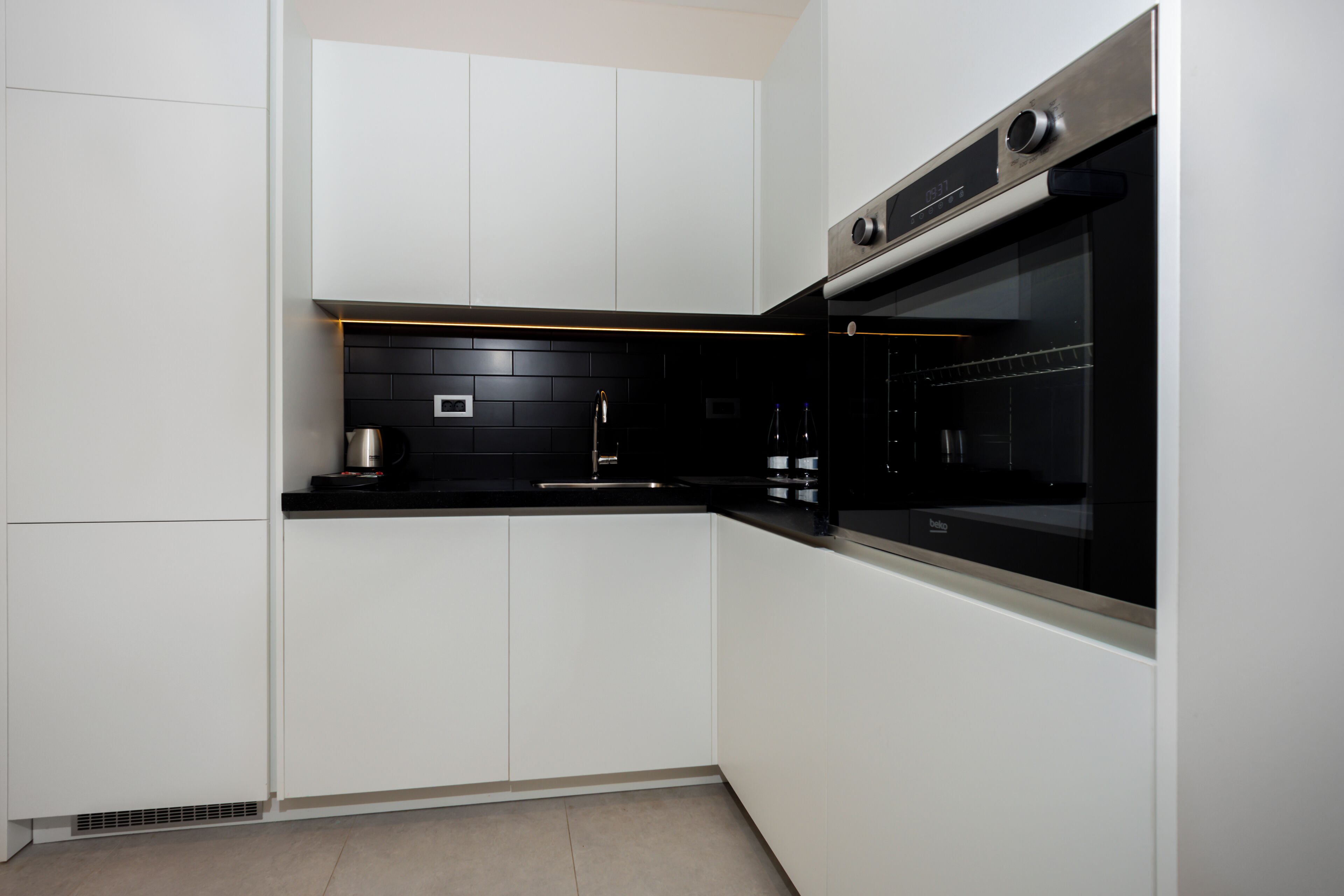 Una cocina moderna con gabinetes blancos, una encimera negra y un horno empotrado.