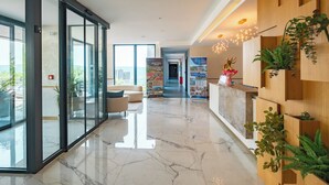 A modern hotel lobby with a marble floor, glass doors, a reception desk, and a view of the outdoors. - Royal Blue Resort & Residence (Kotor)