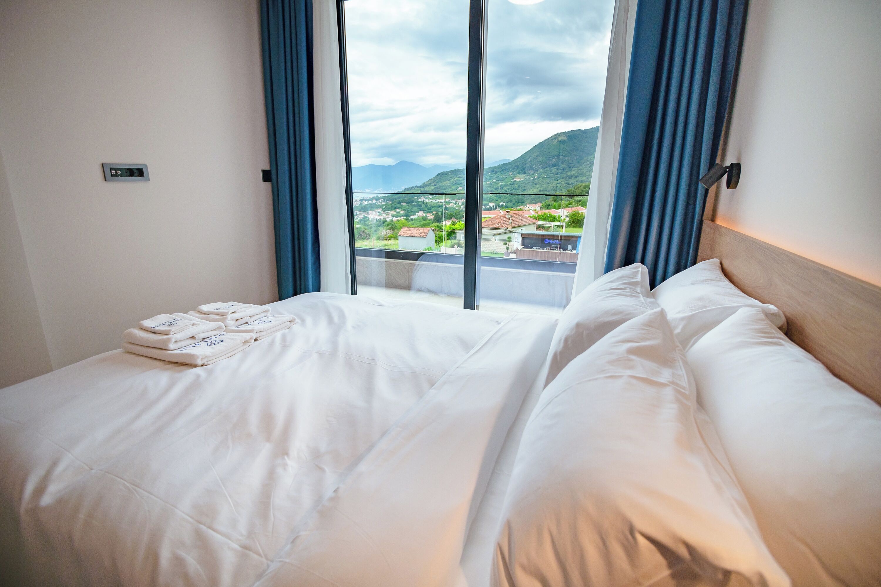 A hotel room with a large bed, a view of a mountainous landscape, and a window with curtains.