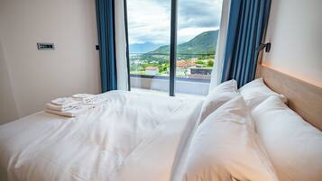 A hotel room with a large bed, a view of a mountainous landscape, and a window with curtains.