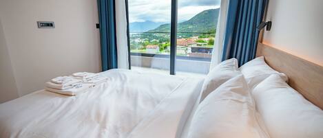 A hotel room with a large bed, a view of a mountainous landscape, and a window with curtains.
