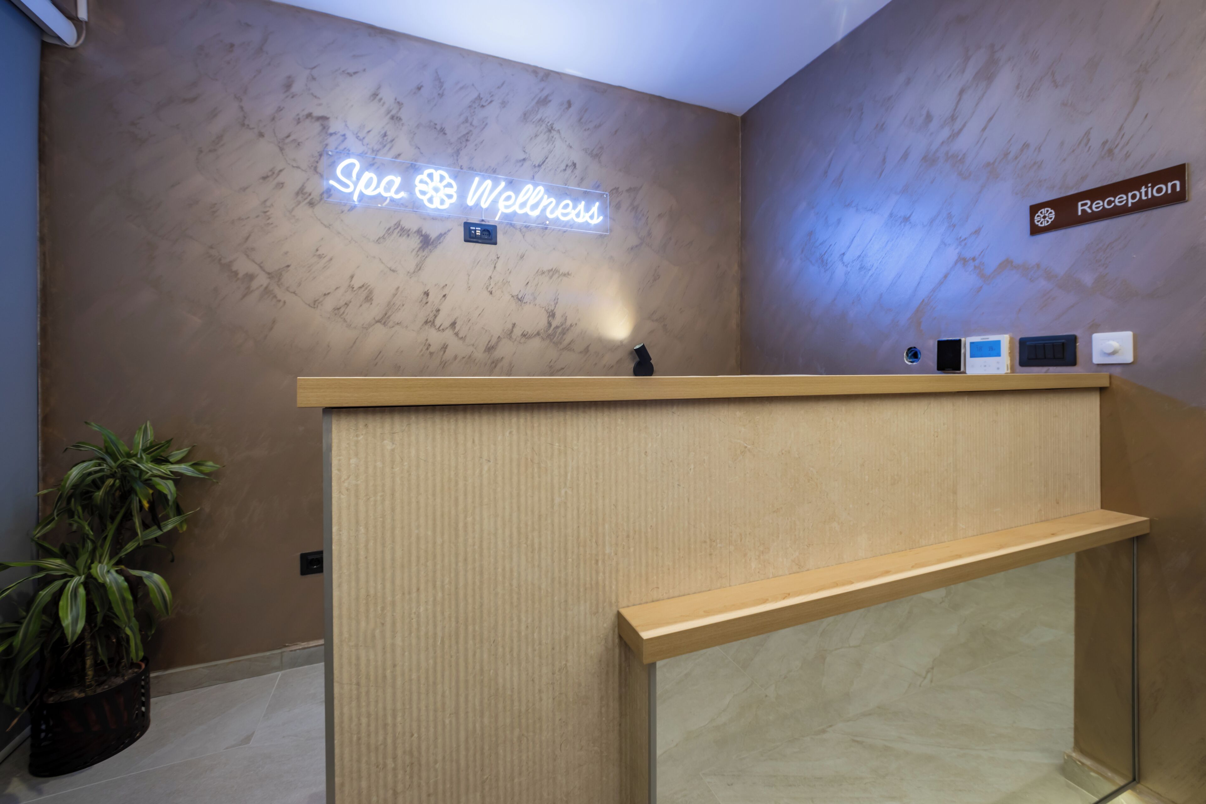 Una mesa de recepción con un letrero de neón que dice 'Spa & Wellness' y un cartel con la palabra 'Recepción' encima.