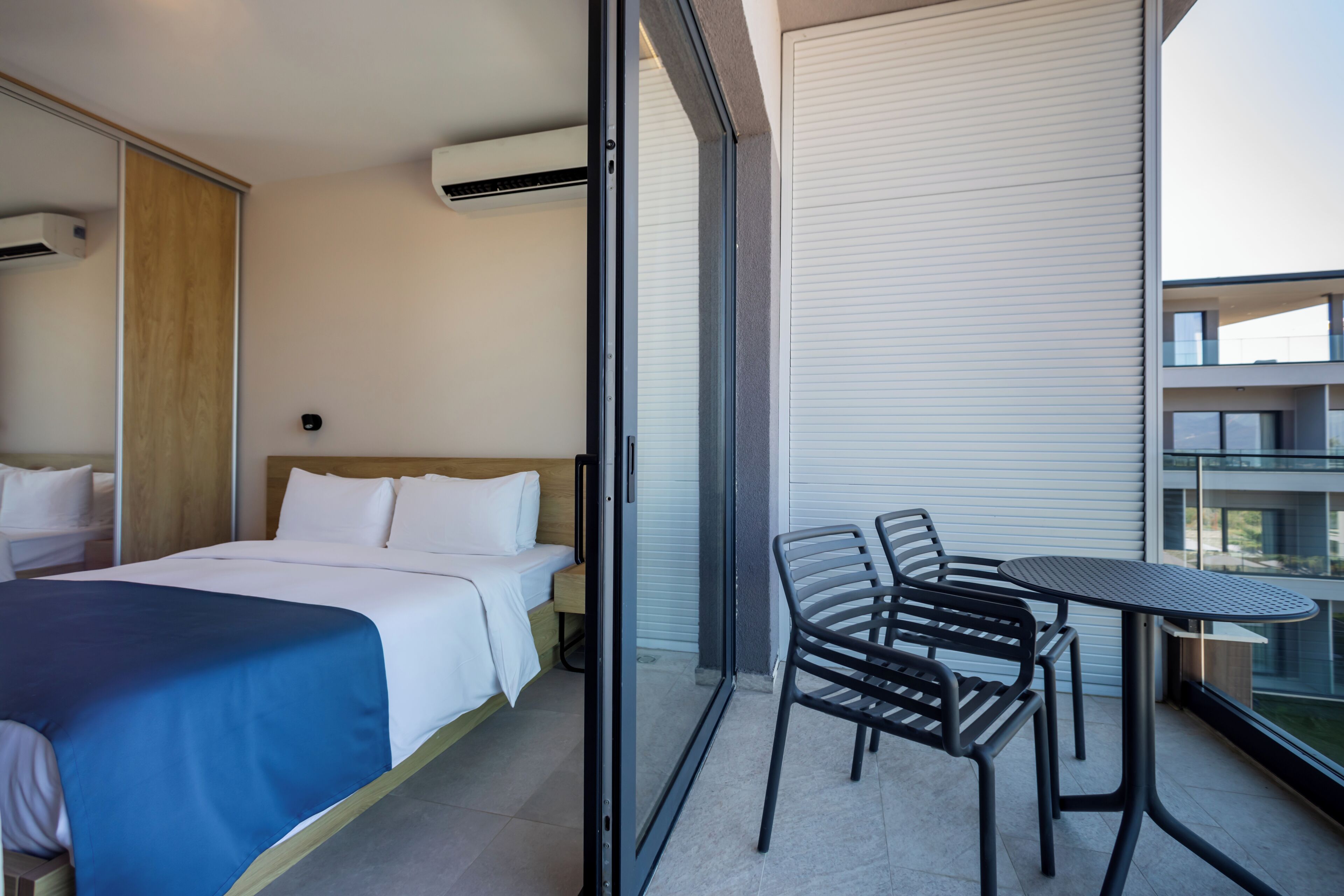 A hotel room with a bed, a small table, and chairs, and a balcony with a view.