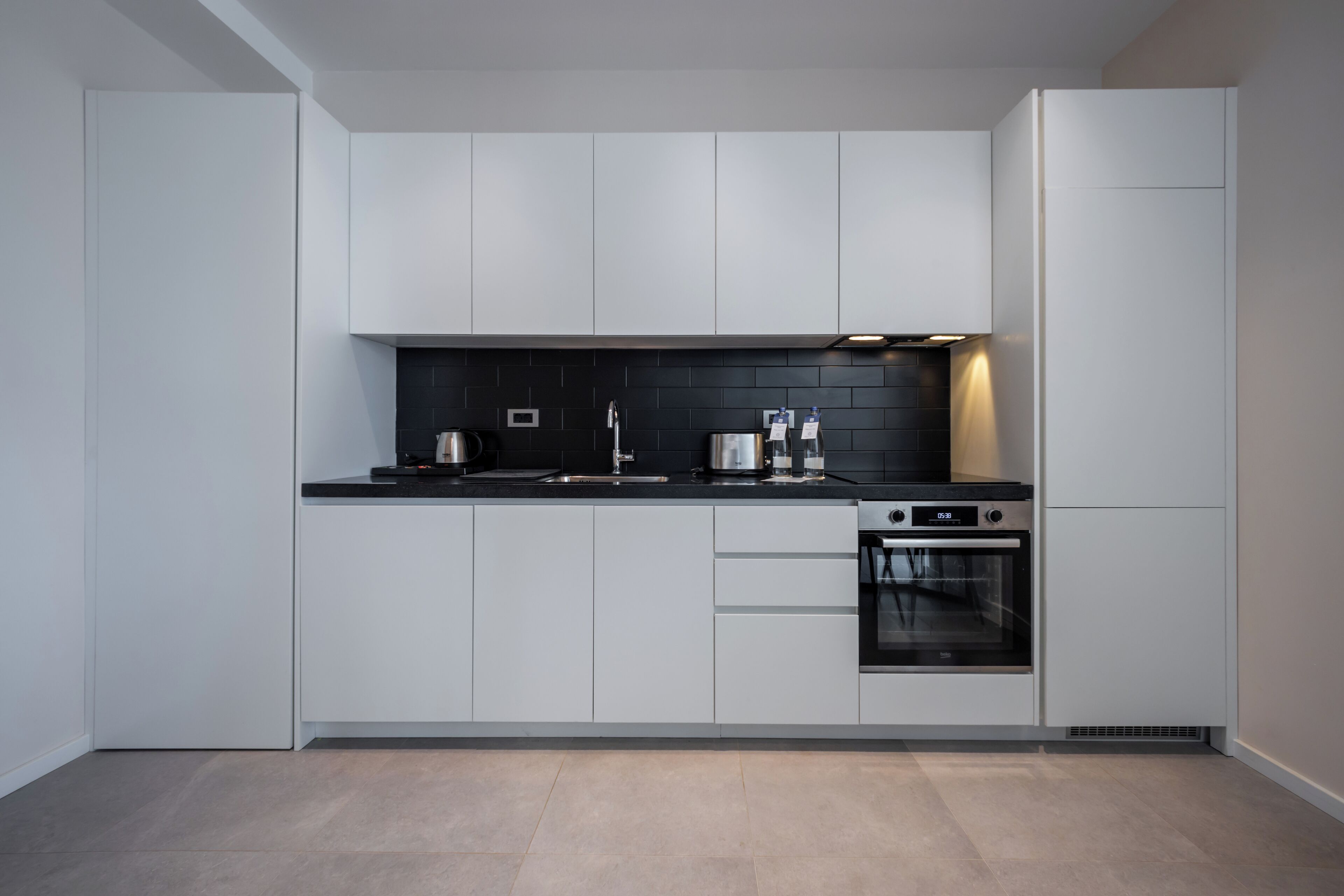 Een moderne keuken met witte kastjes, een zwart aanrecht, een waterkoker, een koffiezetapparaat en een oven.