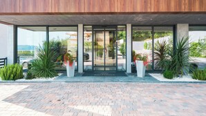 A modern building entrance with a glass door, concrete pillars, and a brick pathway. - Royal Blue Resort & Residence (Kotor)