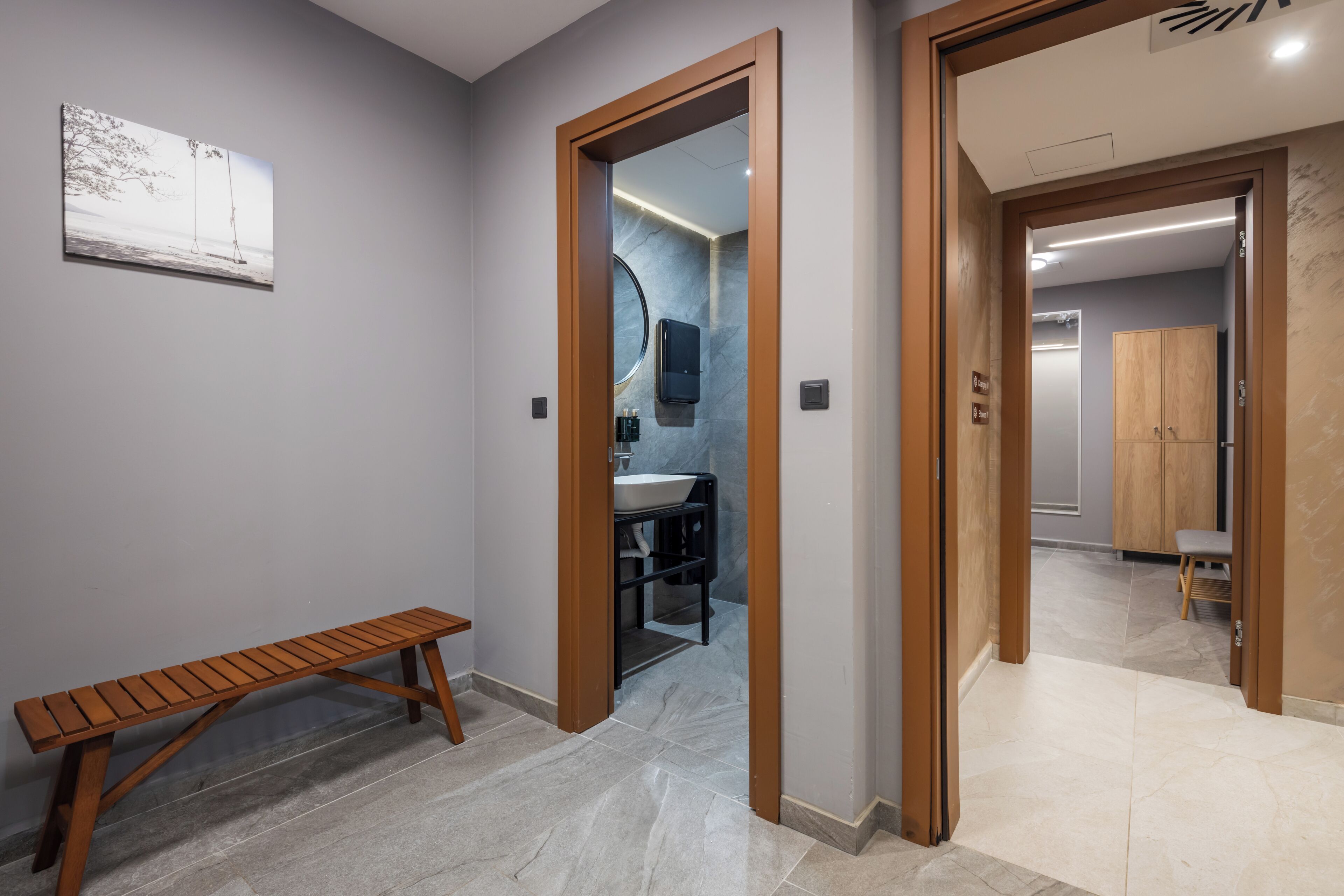 A hallway with a wooden bench, a bathroom with a marble wall, and a view into another room with a wardrobe.