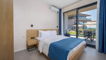 Quarto de hotel com uma cama grande, uma mesinha de cabeceira, uma janela com vista para a área externa e um aparelho de ar condicionado instalado no teto.