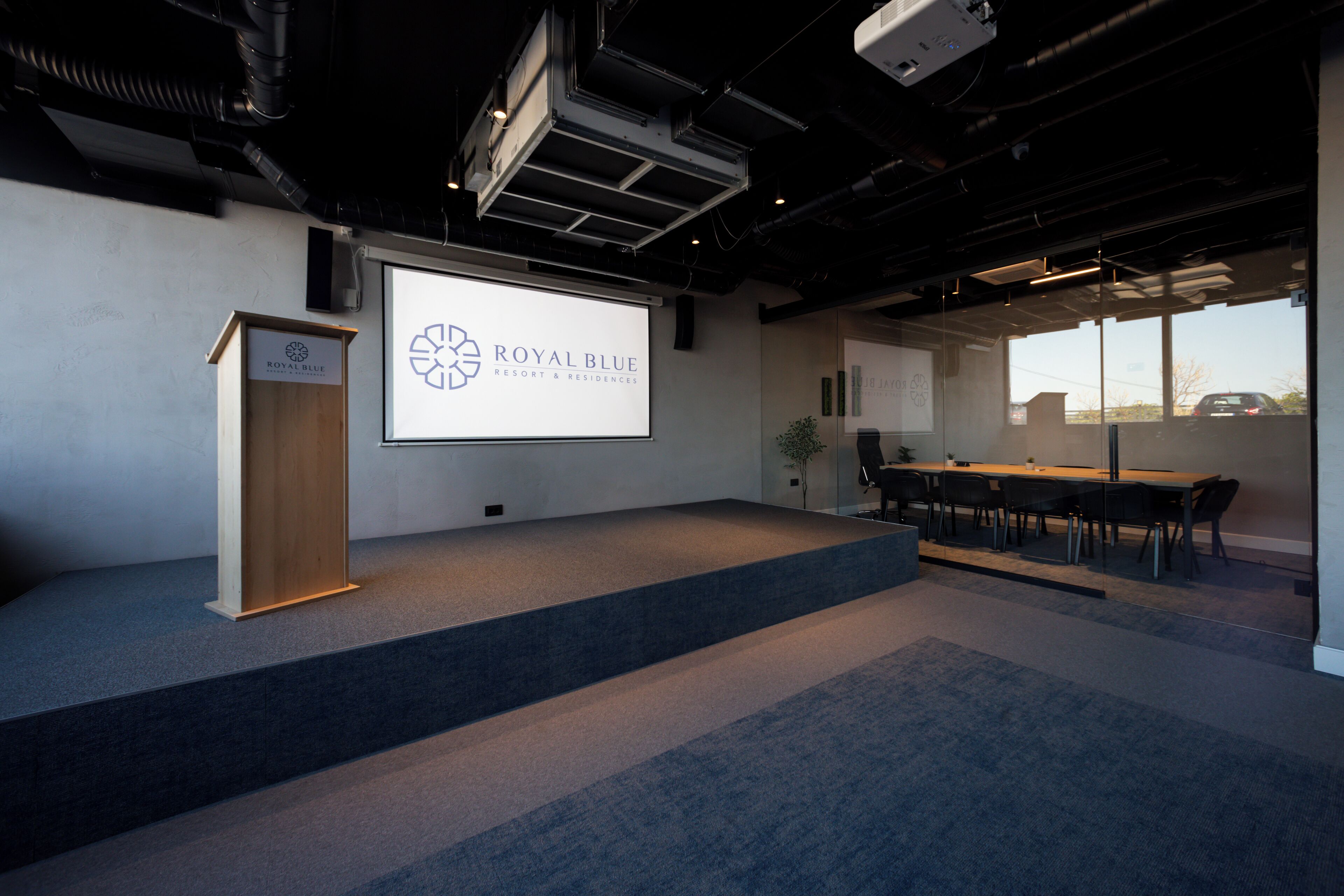 Un salón de conferencias con una pantalla de presentación, un atril y una mesa con sillas.