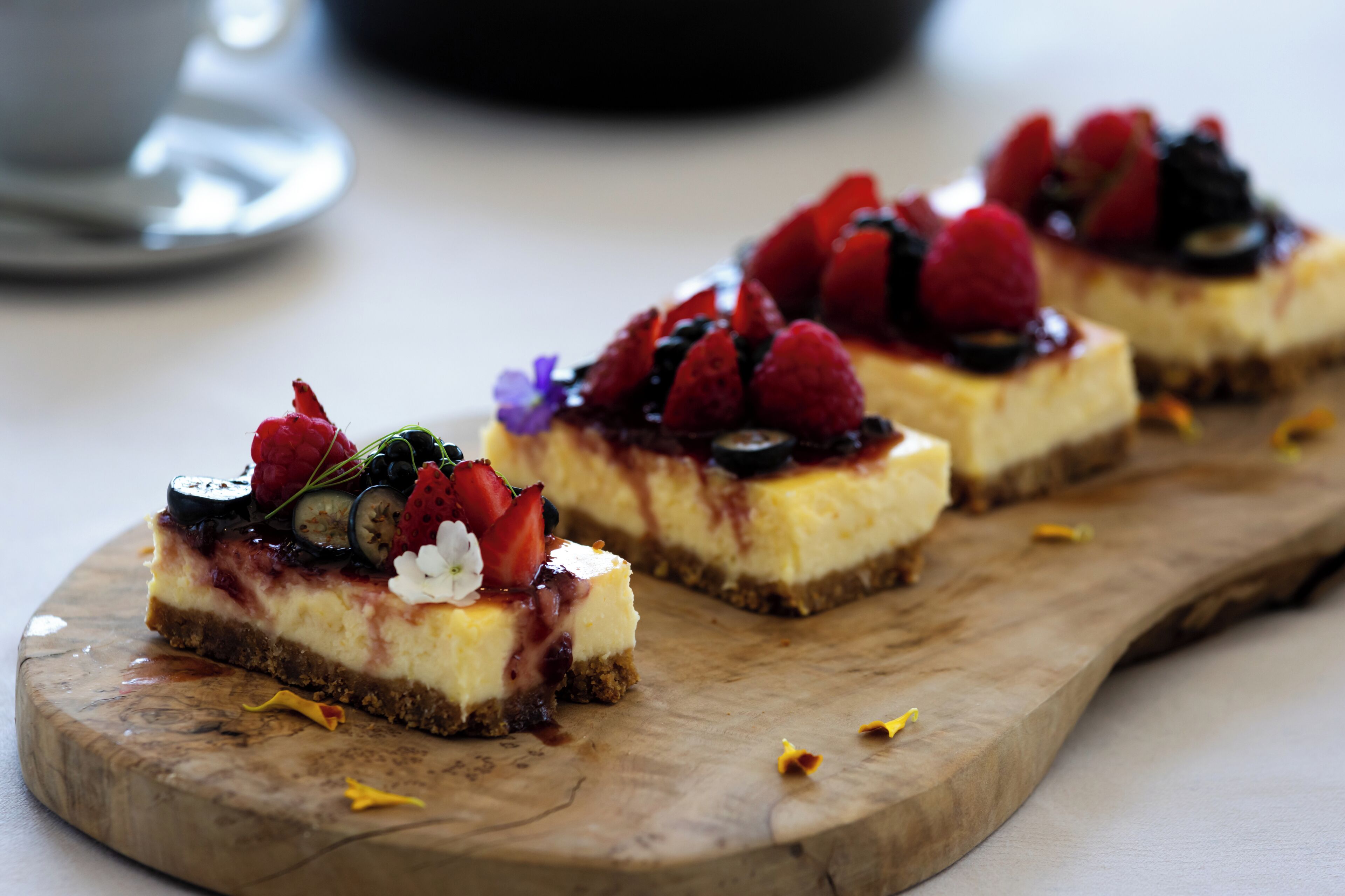 Tres postres cuadrados sobre una tabla de madera, cada uno cubierto de fresas, frambuesas y un hilo de salsa.