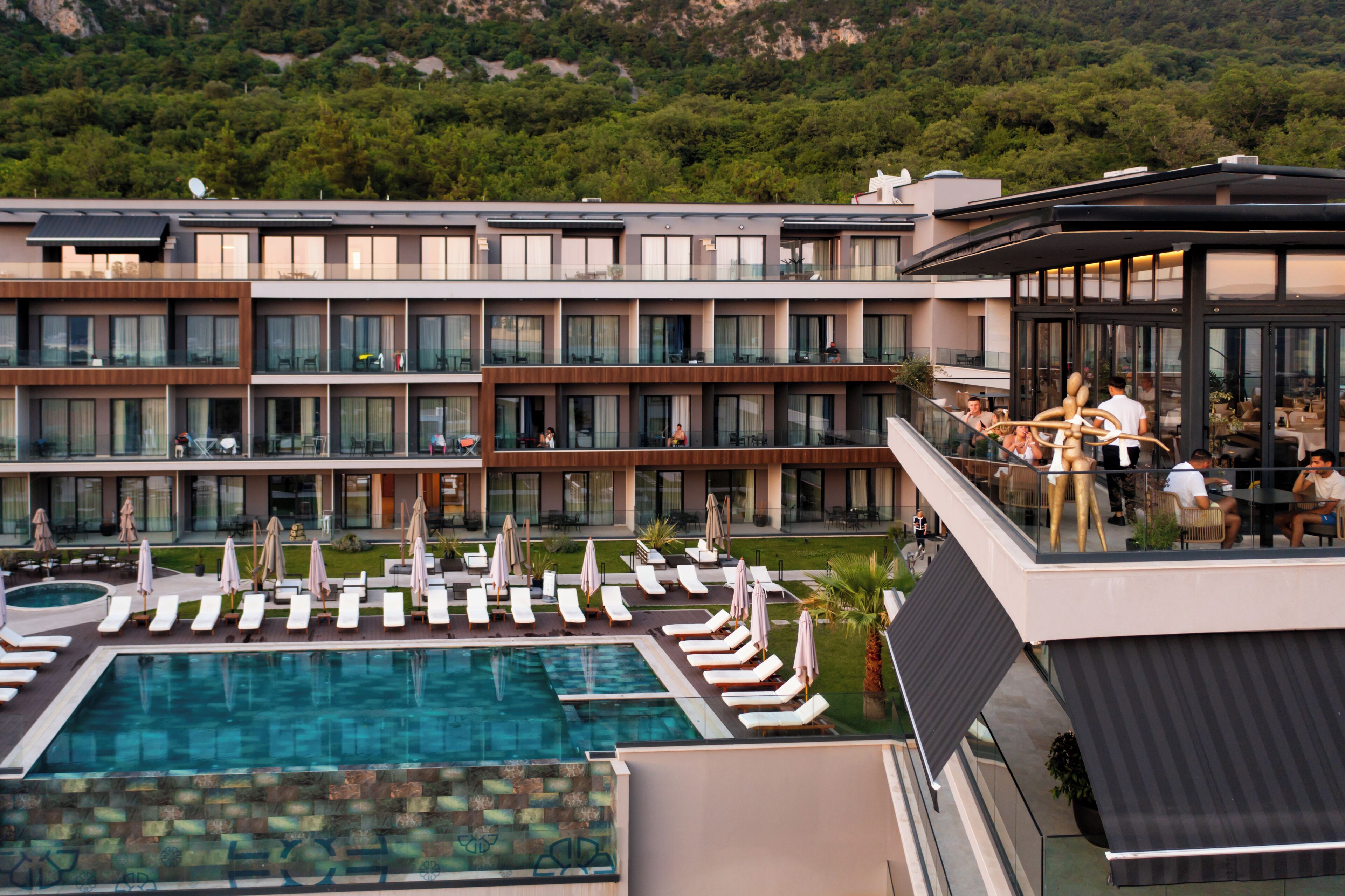 A modern hotel with a pool, multiple balconies, and a restaurant area.
