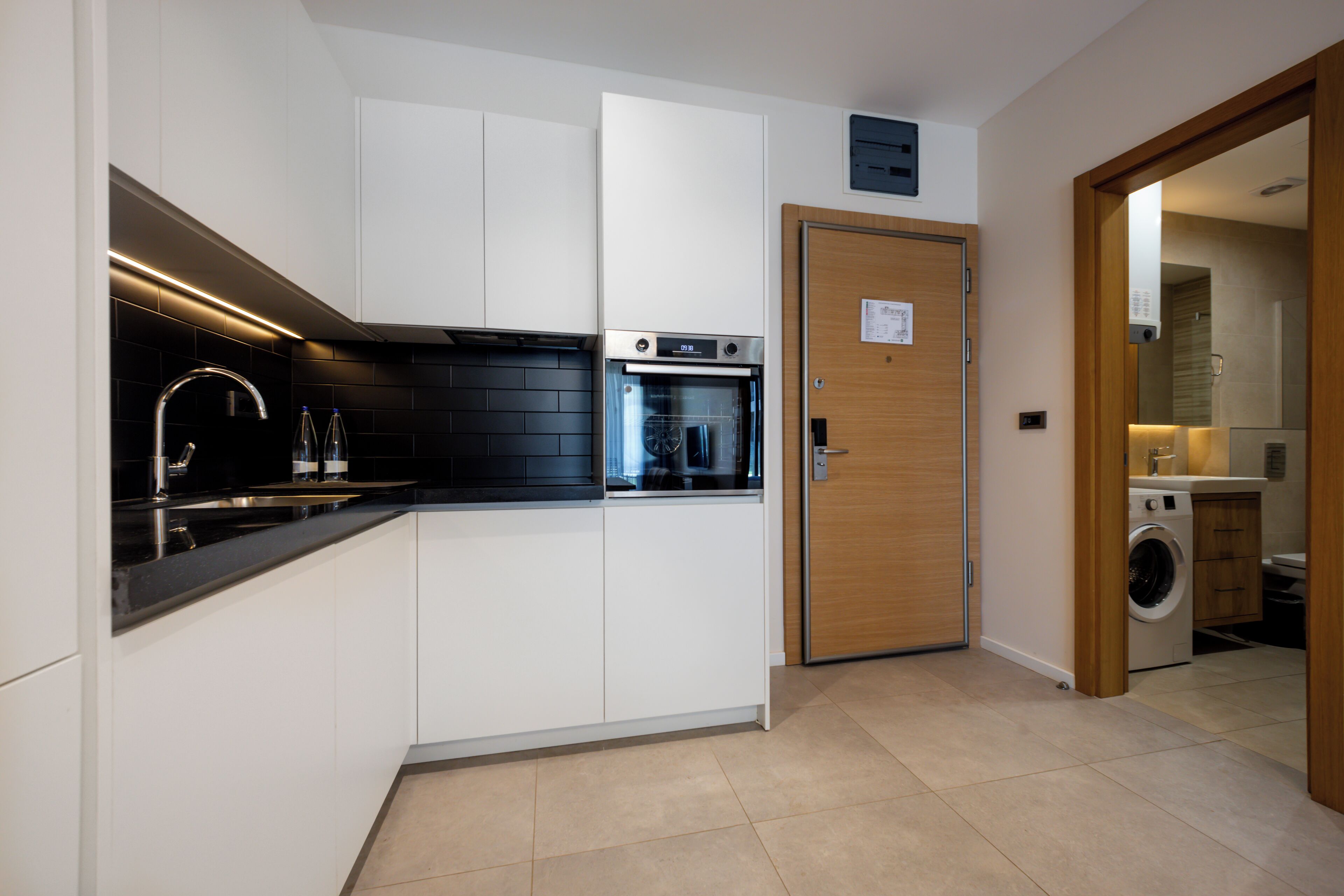 A modern kitchen with white cabinets, a black countertop, an oven, and a washing machine.