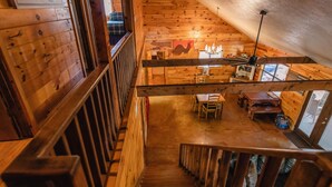A wooden cabin interior with a staircase leading to a dining area. - Quaint home nestled in the heart of Concan Texas! (Concan)