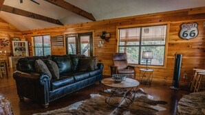 A cozy cabin interior with a leather sofa, a round coffee table, and a cowhide rug. - Quaint home nestled in the heart of Concan Texas! (Concan)