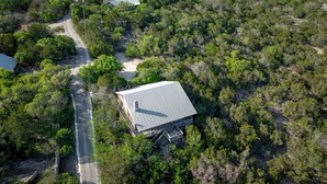 An aerial view of a house surrounded by dense vegetation, with a paved road leading to it. - Spacious home with a great view! (Concan)