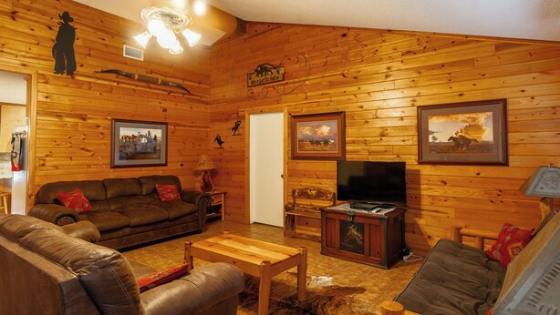 A wooden-paneled living room with a brown leather sofa, a wooden coffee table, and a television.