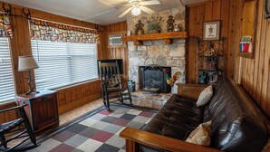 A cozy living room with a fireplace, wooden walls, and a checkered floor.