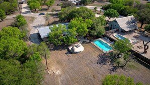 An aerial view of a residential property with a swimming pool, a covered patio, and a fenced yard.