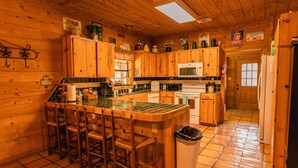 A wooden cabin-style kitchen with a central island, bar stools, a microwave, and a refrigerator. - Great Vacation Home with wrap around porch (Concan)