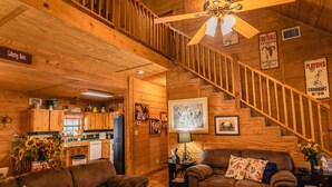 A cozy wooden cabin interior with a living room, kitchen, and a staircase. - Great Vacation Home with wrap around porch (Concan)