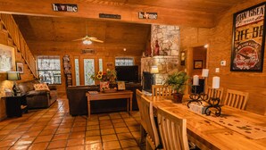 A cozy, rustic living room with a fireplace, wooden furniture, and a staircase leading to another level. - Great Vacation Home with wrap around porch (Concan)