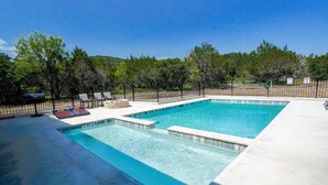 A rectangular swimming pool with a black metal fence, lounge chairs, and a barbecue grill. - New custom home located in the Mountain Valley subdivision (Concan)