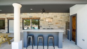 A modern kitchen with a stone backsplash, a white countertop, and three bar stools. - New custom home located in the Mountain Valley subdivision (Concan)
