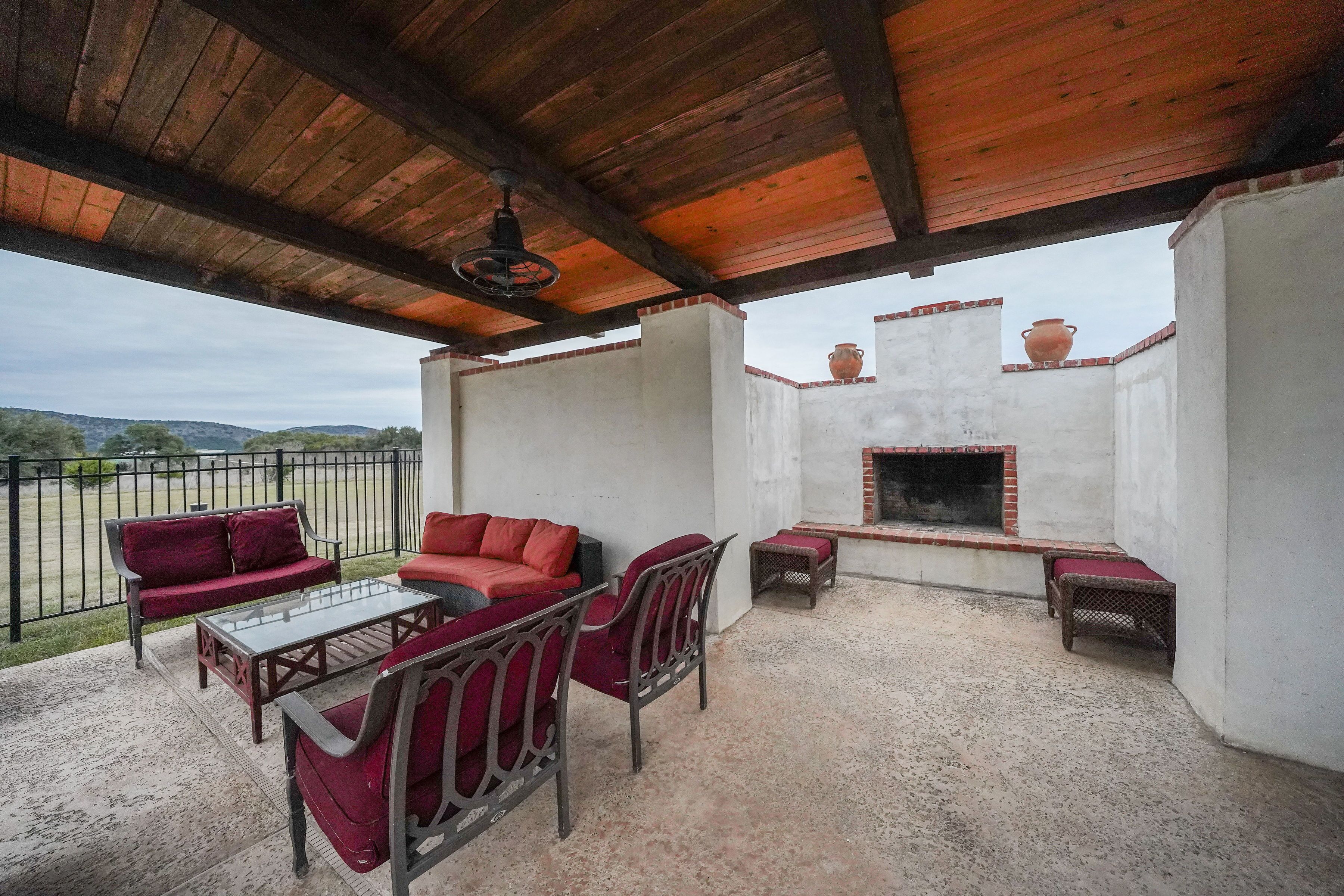 An outdoor patio with a wooden ceiling, red cushioned seating, a glass table, and a brick fireplace.