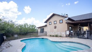 A swimming pool with a stone border, a building with a star logo, and a fenced patio area. - Spacious home located in Mountain Valley (Concan)