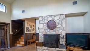 A spacious living area with a stone fireplace, a television, and a wooden bench. - Spacious home located in Mountain Valley (Concan)
