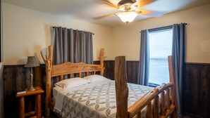 A bedroom with a wooden bed frame, a ceiling fan, a bedside lamp, and a window with curtains. - Spacious home located in Mountain Valley (Concan)