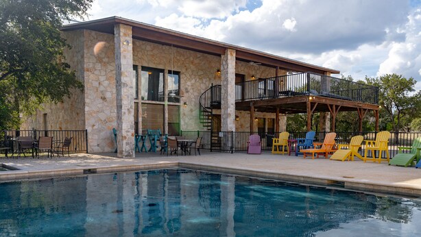 A pool area with a stone building, outdoor seating, and a covered patio with chairs. - Large Lodge located in Mountain Valley (Concan)