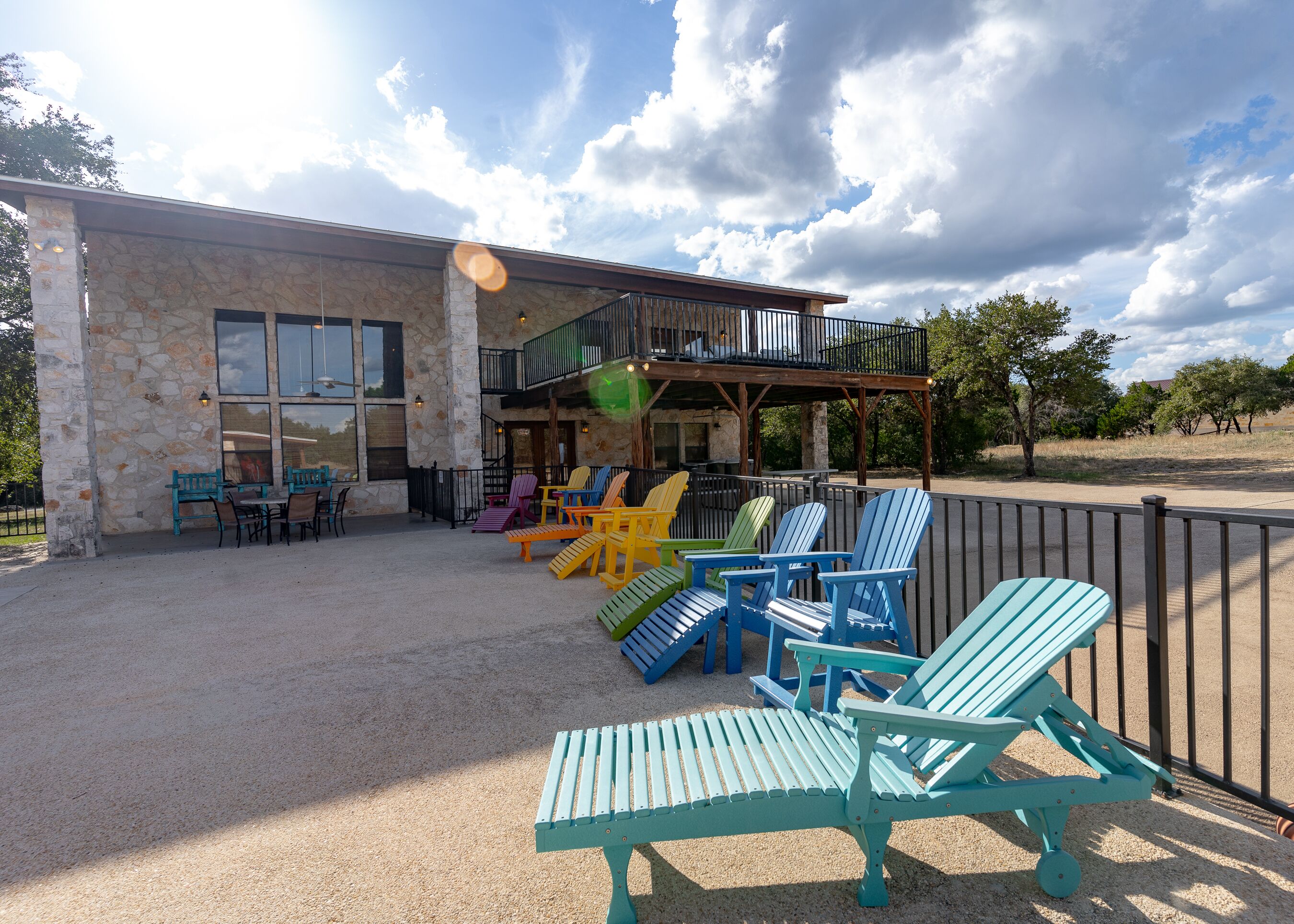 Un edificio con fachada de piedra, zona de estar al aire libre con sillas Adirondack de colores y un balcón con vistas al patio.