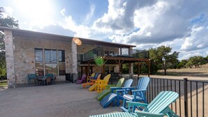 A building with a stone facade, outdoor seating area with colorful Adirondack chairs, and a balcony overlooking the patio. - Large Lodge located in Mountain Valley (Concan)