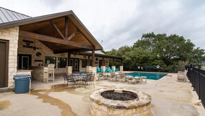 A covered patio area with stone walls, outdoor seating, a swimming pool, and a fire pit. - Beautiful Vacation Home with GREAT amenities (Concan)