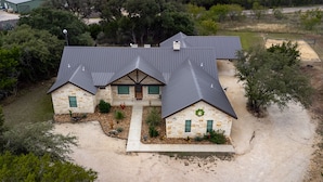 A two-story house with a stone facade, a dark roof, and a front yard with landscaping. - Beautiful Vacation Home with GREAT amenities (Concan)