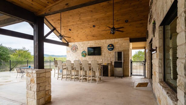 A covered outdoor area with stone pillars, a stone wall, a television, and a bar area with chairs. - Beautiful Vacation Home with GREAT amenities (Concan)