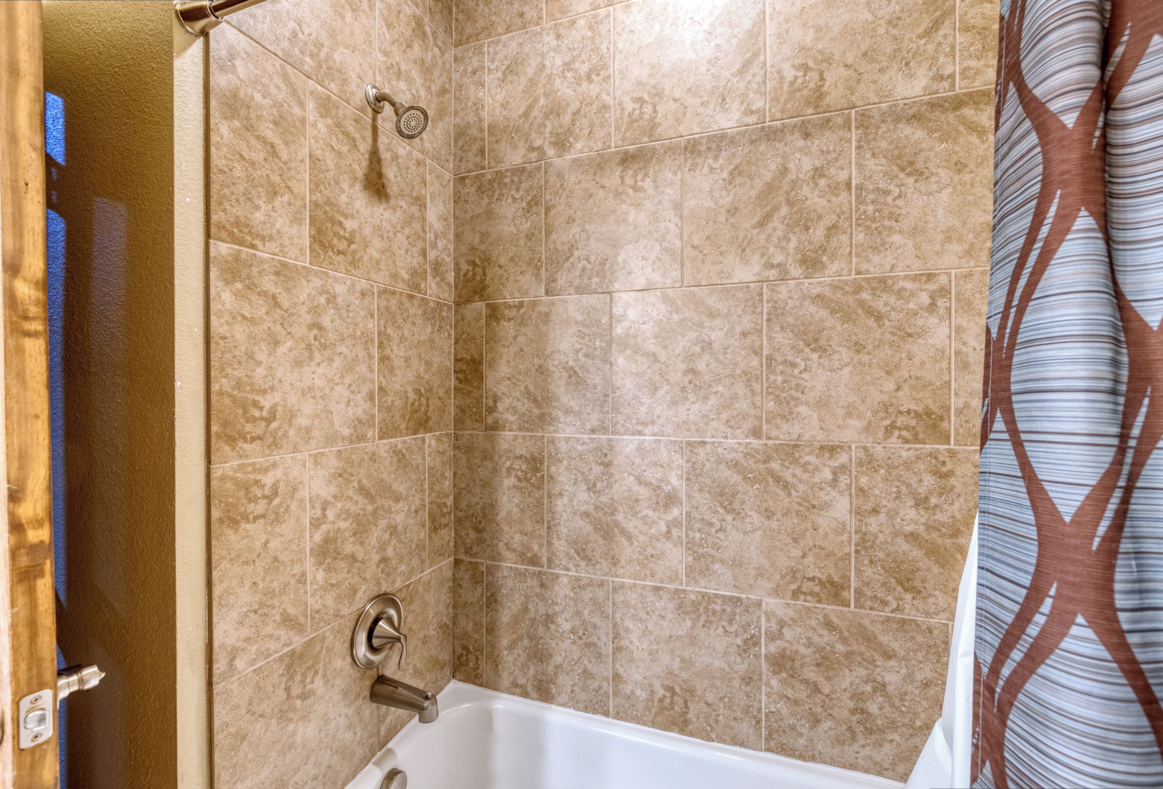 A bathroom with beige tiles, a bathtub, and a shower head.