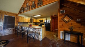 L’intérieur d’une cabane en rondins comprend une cuisine, un coin repas et une cheminée en pierre.