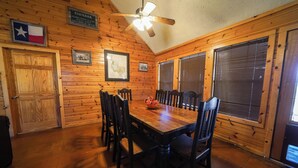 Une pièce aux murs lambrés, comprenant une table à manger, des chaises, un ventilateur de plafond et un drapeau du Texas.