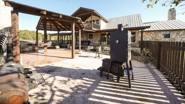 Un patio couvert avec un bâtiment en pierre, un barbecue et une clôture en bois.