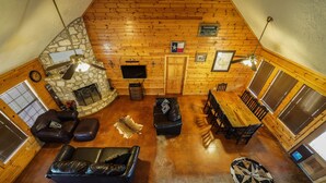 L’intérieur chaleureux d’un chalet avec une cheminée en pierre, des fauteuils en cuir, une table à manger en bois et un ventilateur de plafond.