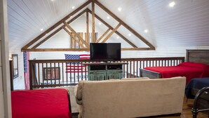 A cozy loft-style room with a high ceiling, wooden beams, a television, and red and beige upholstered seating. - Farmhouse - located on the 18th Hole (Concan)