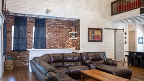 A spacious living room with a large leather sectional sofa, a wooden coffee table, and a brick accent wall. - Farmhouse - located on the 18th Hole (Concan)