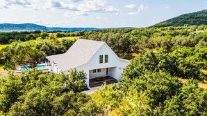 A white house with a steep roof, surrounded by dense greenery and hills in the background. - Farmhouse - located on the 18th Hole (Concan)