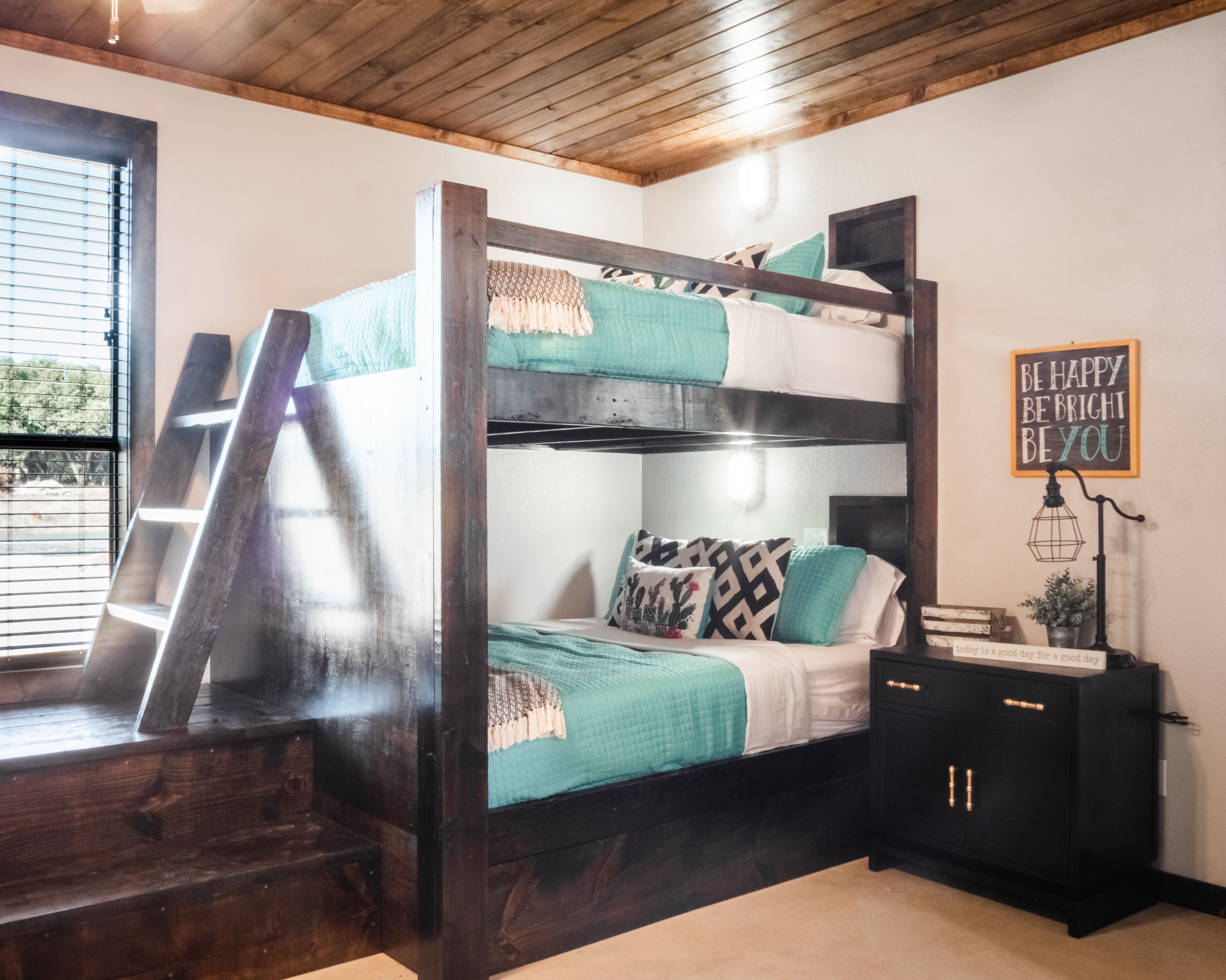 A bunk bed with a ladder, a bedside table with a lamp, and a motivational quote on the wall.